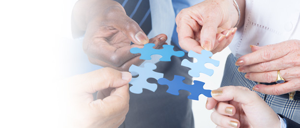 four people's hands holding a puzzle piece.